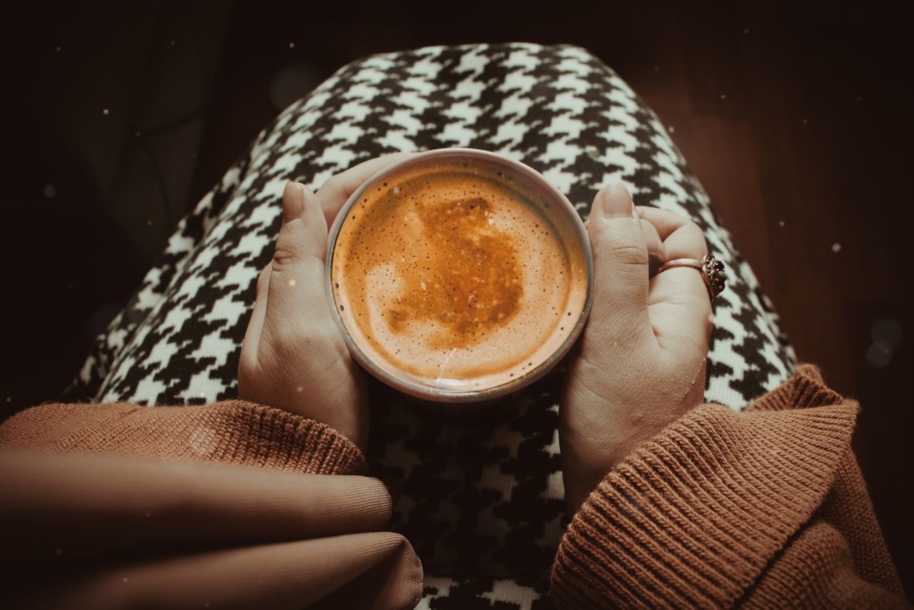 A warm cappuccino held in cozy hands on a houndstooth lap, perfect for a relaxing autumn day.